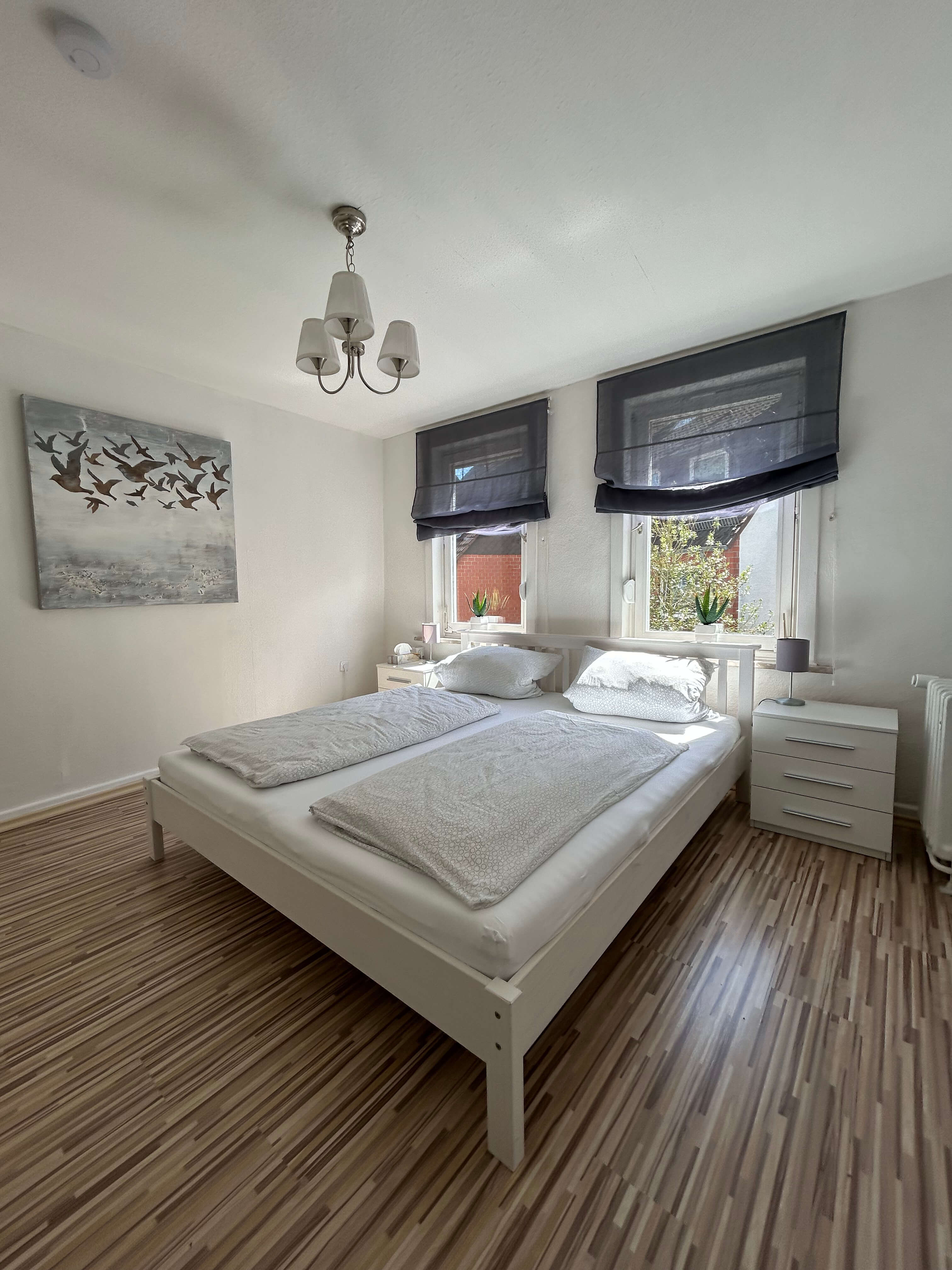 Quartier 26 – Schlafzimmer mit weißem Doppelbett und Vogel-Kunstwerk